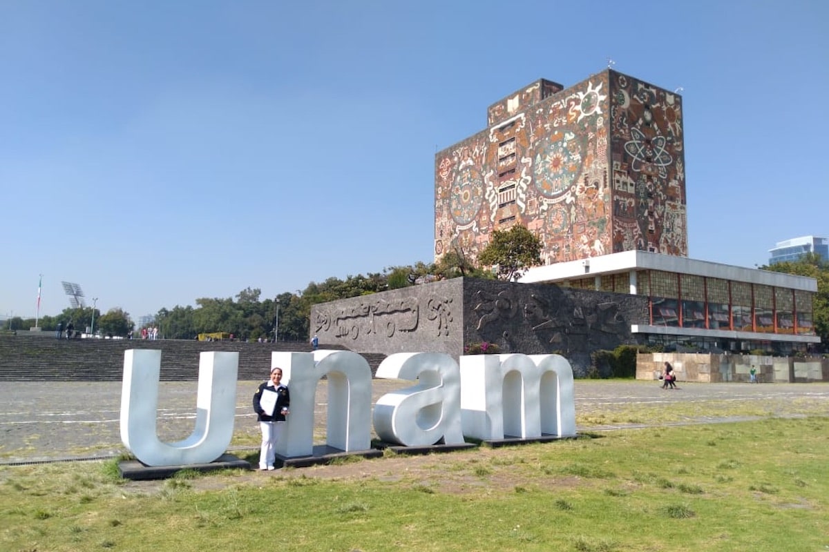 Alumna sosteniendo reconocimiento junto a letrero UNAM